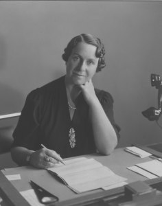 Haslett, Dame Caroline - seated at desk